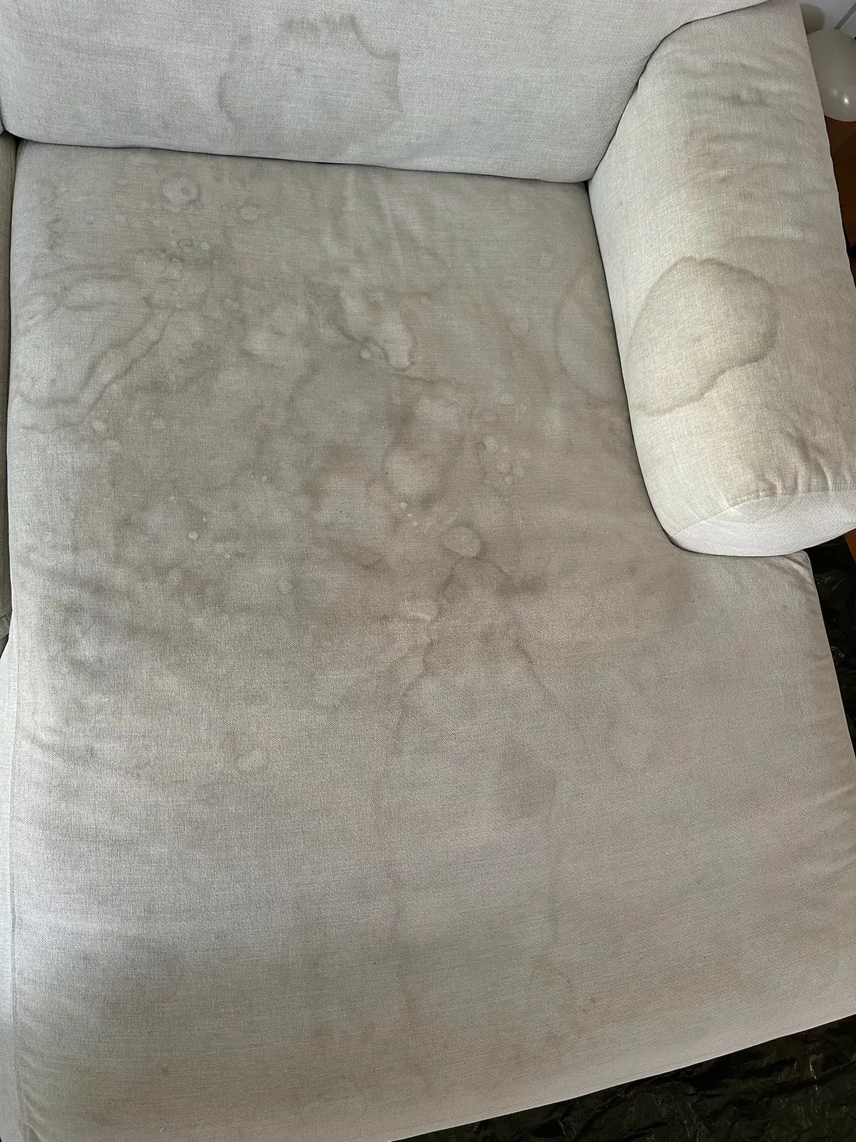 Helles Stoffsofa mit eingetrockneten Flüssigkeitsrändern auf der Sitzfläche vor der Polsterreinigung